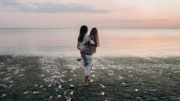 Moeder met dochter op de arm op het strand met een ondergaande zon