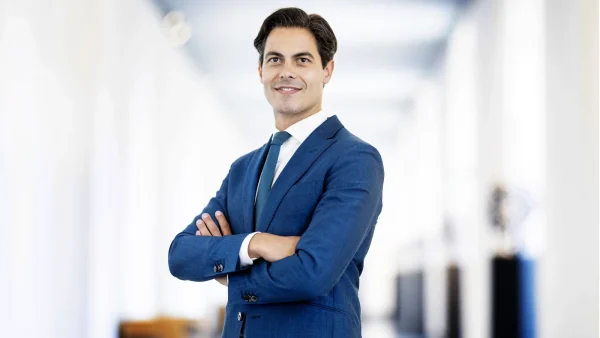 Rob Jetten staat in een blauw pak met zijn armen over elkaar