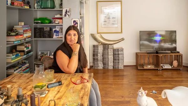 Marguerite zit aan haar eettafel, drie grote stapels met LINDA.'s achter haar