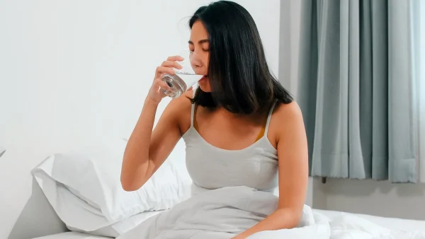 Vrouw drinkt glas water in bed nadat ze melatonine heeft geslikt