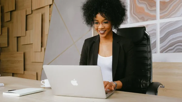 Foto van een vrouw van kleur die lachend achter haar laptop zit