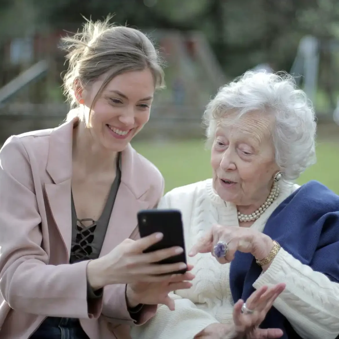 Een vrouw zit samen met een oudere vrouw op een bankje | Ter illustratie van mantelzorger