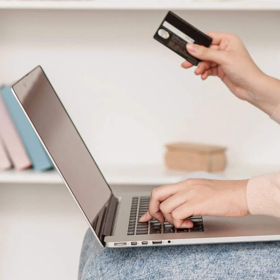 Vrouw shopt online via laptop met bankpas in rechter hand
