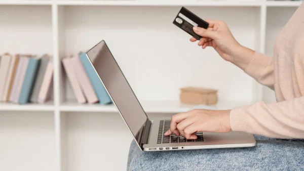 Vrouw shopt online via laptop met bankpas in rechter hand