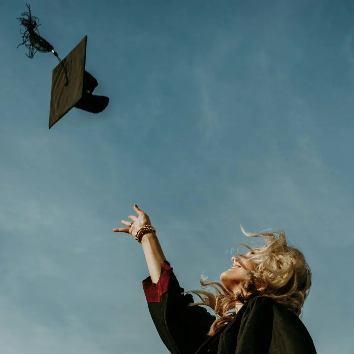 Vrouw gooit graduation cap in de lucht na behalen van master diploma