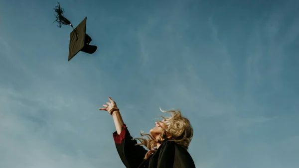 Vrouw gooit graduation cap in de lucht na behalen van master diploma