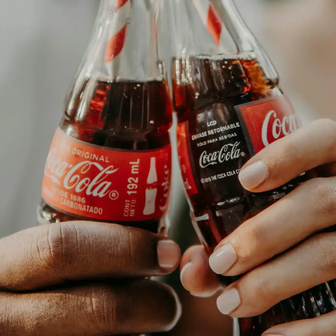 Twee mensen houden een flesje Coca-Cola vast