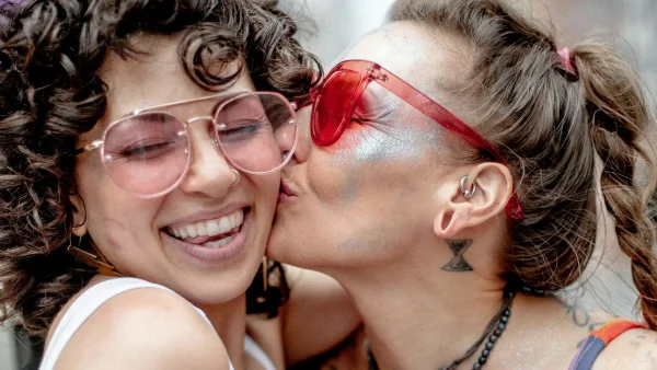 Een vrouw zoent een andere vrouw op de wang tijdens Pride