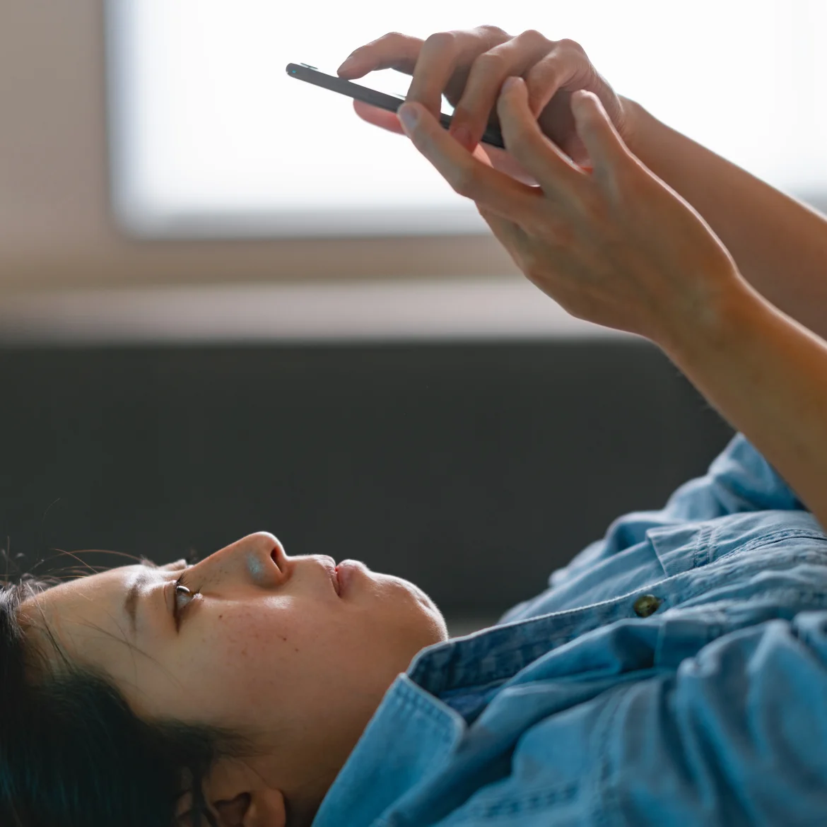 Vrouw ligt op bed met telefoon boven hoofd