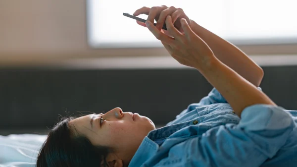 Vrouw ligt op bed met telefoon boven hoofd