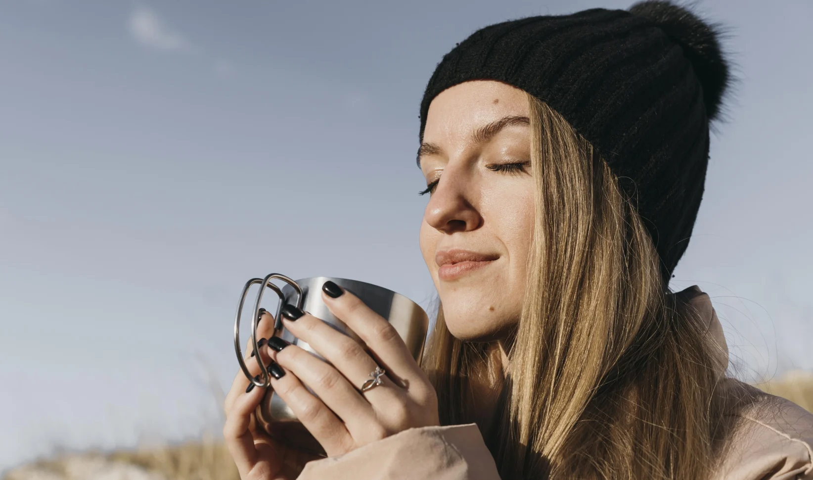 vrouw met warm drankje in de zon | Warme winterjas mét zonnebril: dit wordt het weer dit weekend